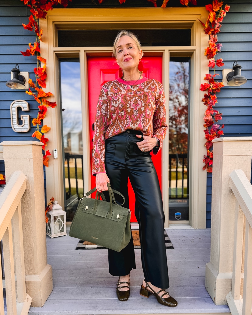 Thanksgiving outfit idea for women over 50. Woman wearing faux leather pants and printed sweater.