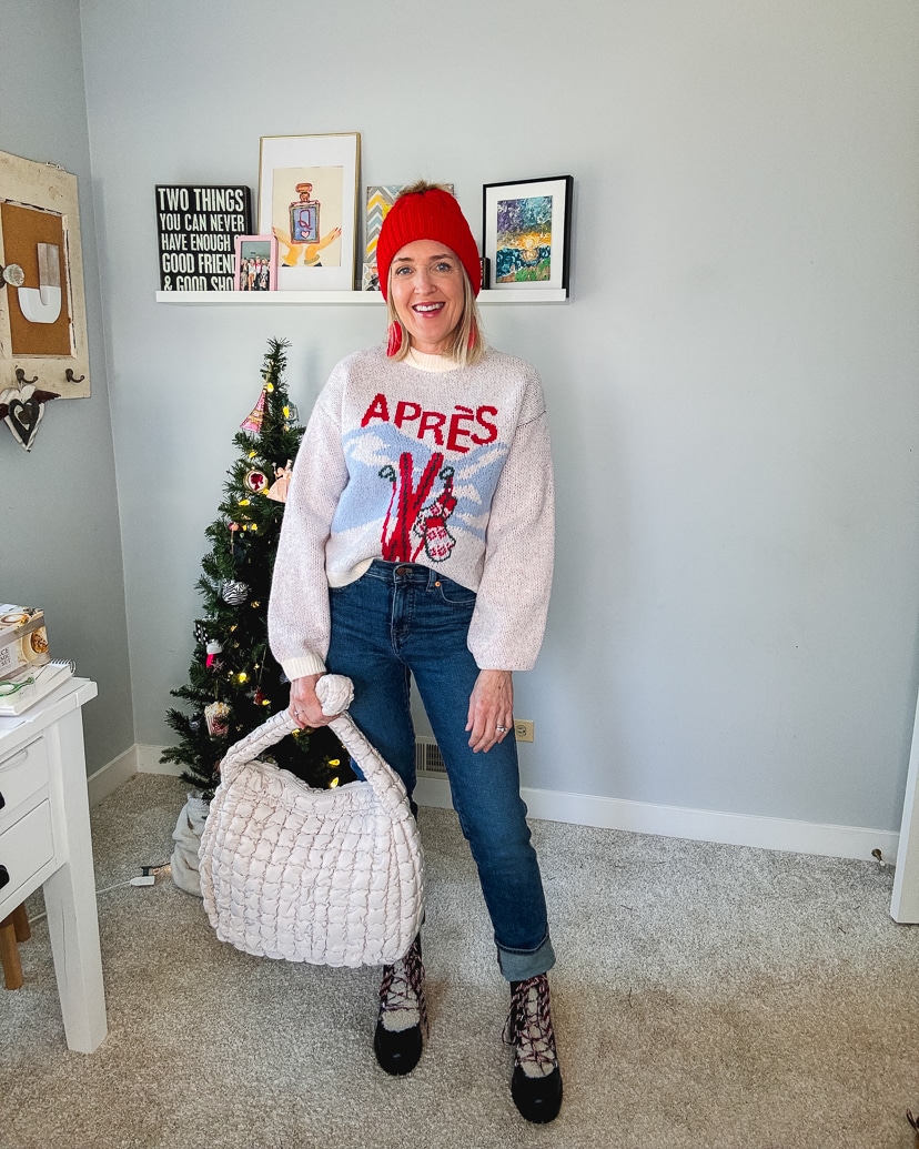 woman wearing a casual holiday outfit - apres sweater, denim, hiking boots and a red beanie