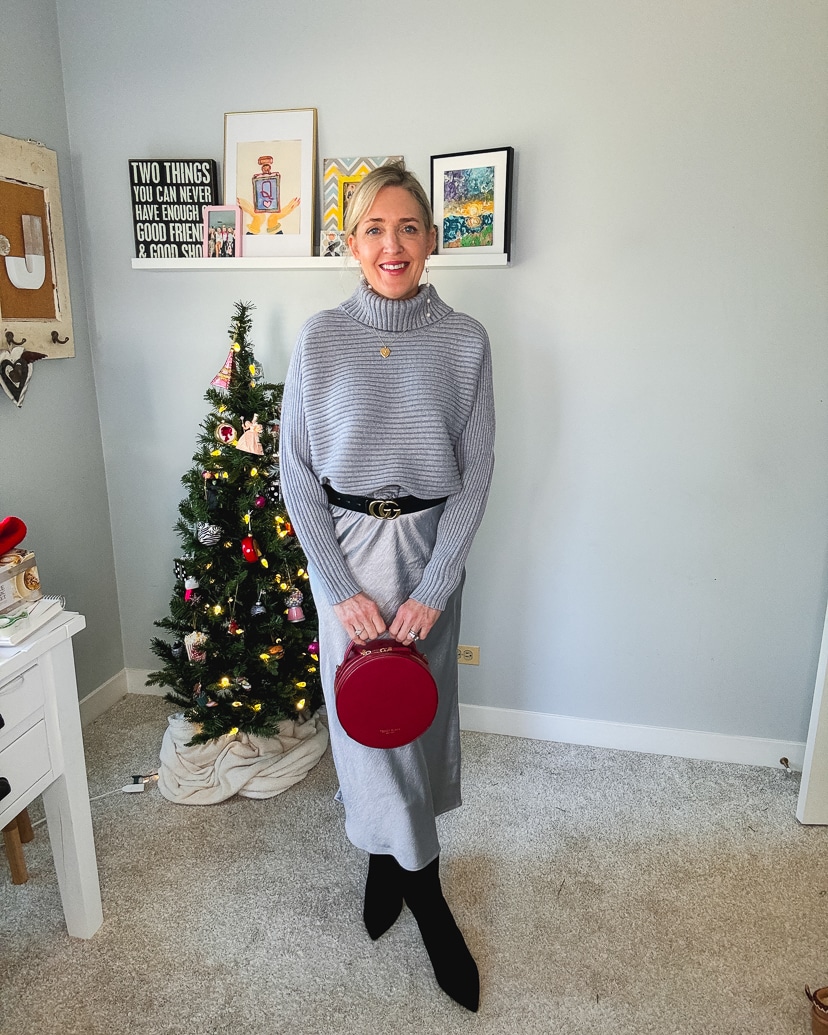 women wearing a festive party outfit - grey sweater, silver slip skirt, black boots and a red handbag.