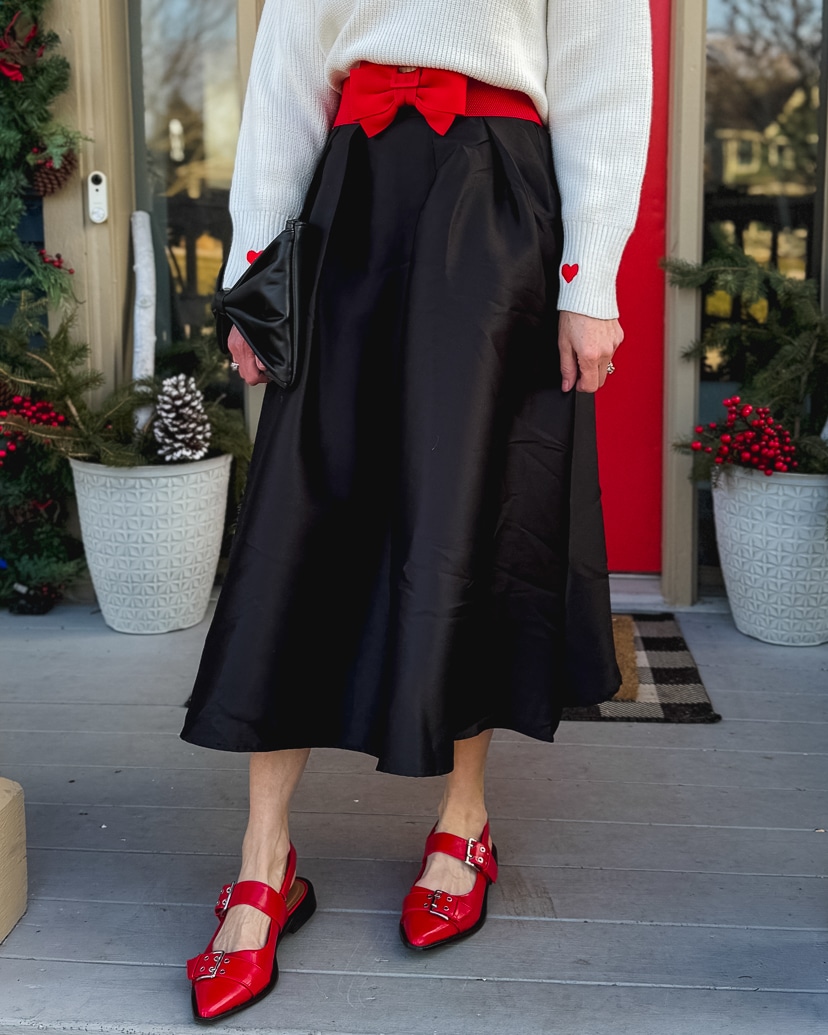 warm and festive holiday outfit idea with a white sweater, black midi skirt, red bow belt and red flats